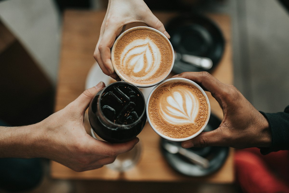 Mãos a segurar cafés com arte latte